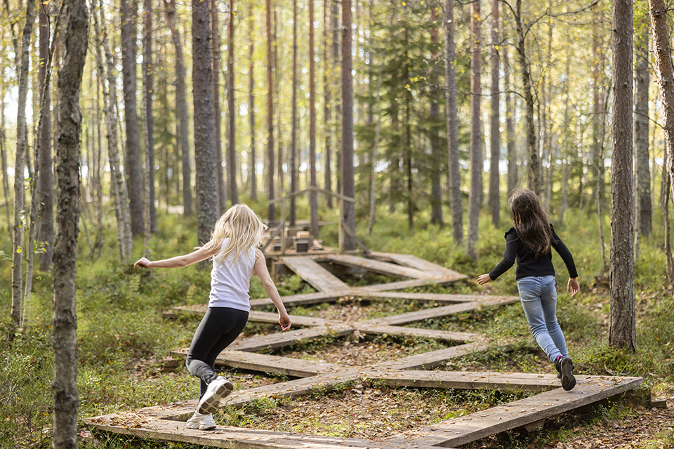 Två flickor springer på spång i skogen.