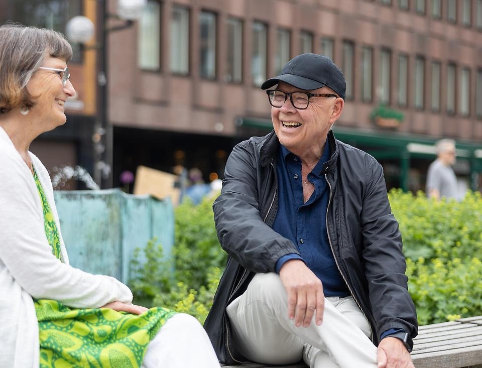 Två glada personer i samtal på en bänk