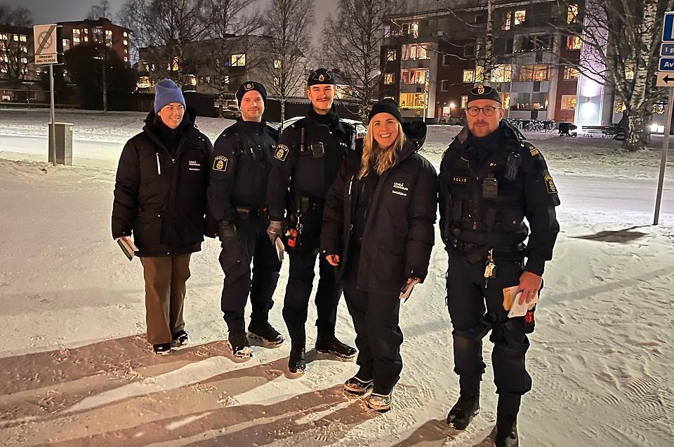 Två socialsekreterare och tre poliser utomhus på vintern i ett bostadsområde.