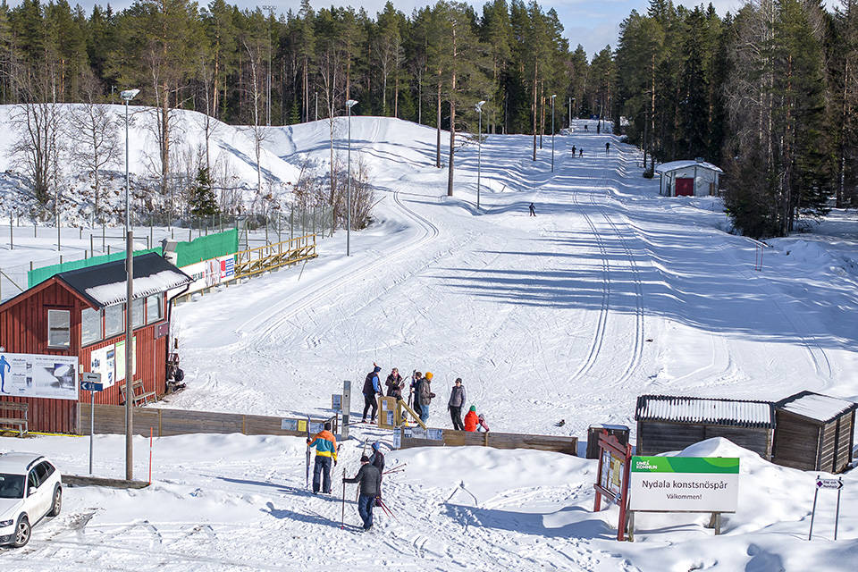 Spårstart på Nydala konstsnöspår. Männsikor på skidor som köar för att få komma in och åka skidor. Mycket snö på backen.