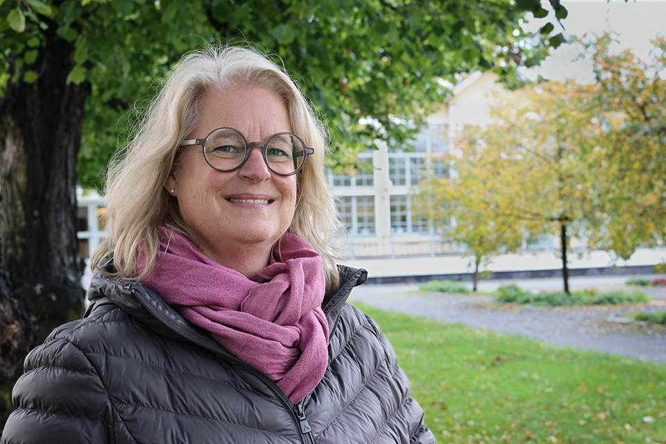 En leende Lena Risholt, systemutvecklare på Umeå kommun, står i den höstvackra parken framför Umeås stadshus.