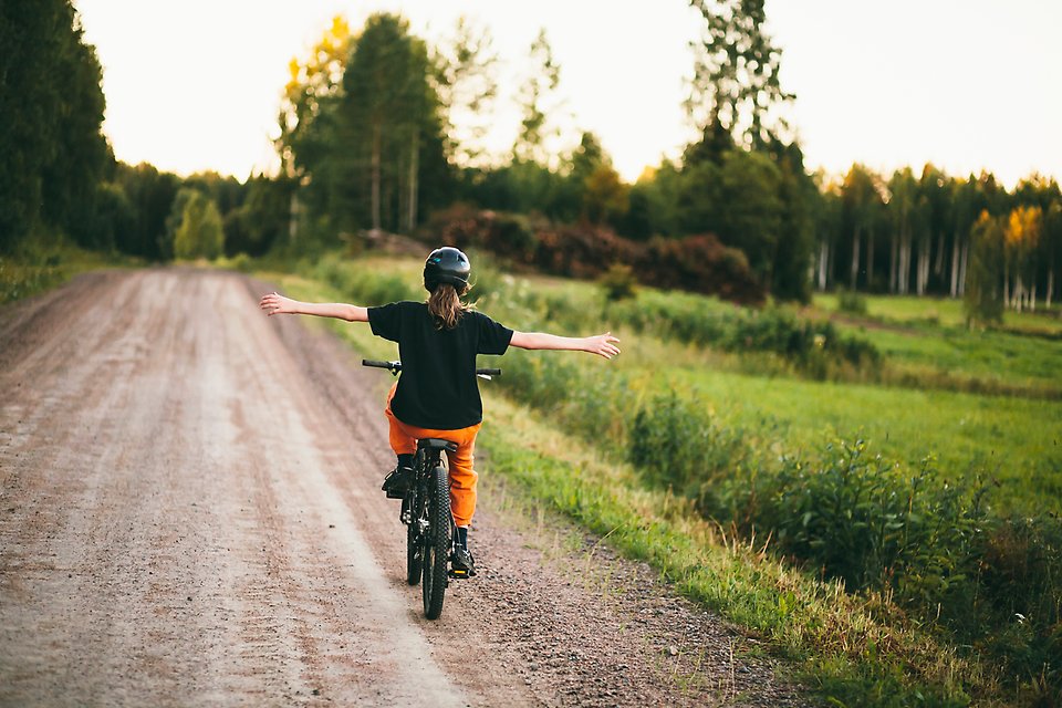 Barn cyklar på grusad landsväg på sommaren.