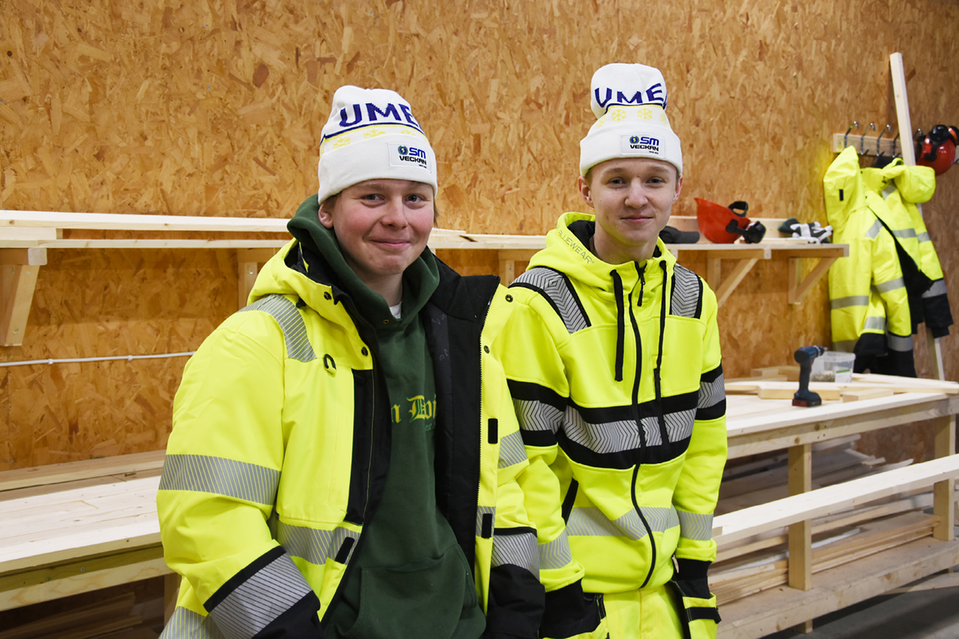 Två ungdomar poserar framför kamera med en vit SM-mössa på huvudet.