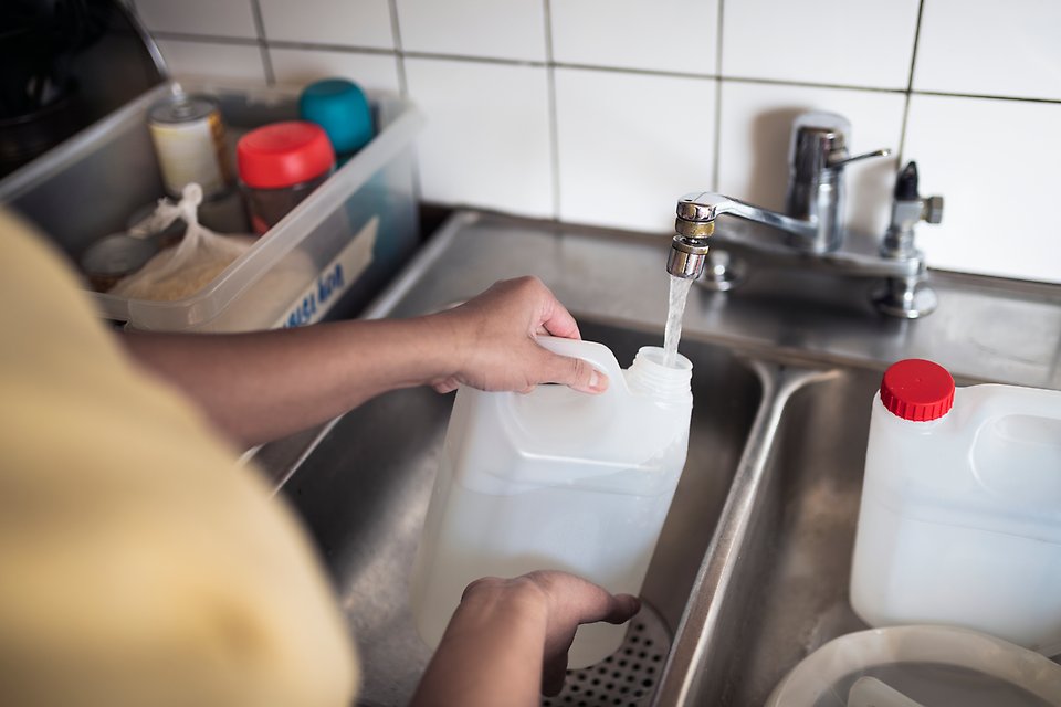 Person fyller på vattendunk med vatten från en kökskran.